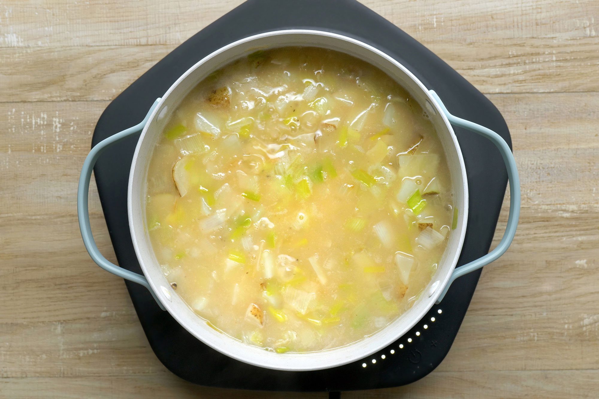 overhead shot; wooden background; Stired in potatoes and leek mixture in to the saucepan;