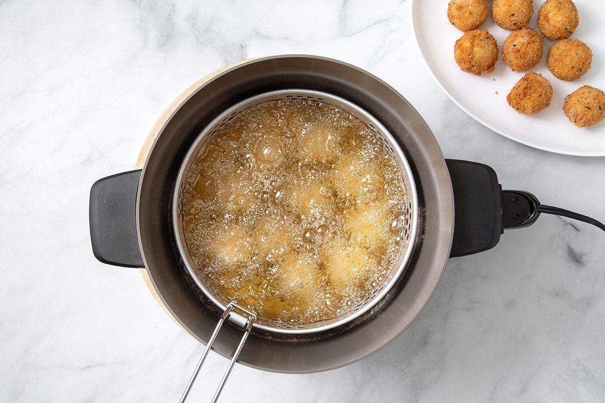 Sauerkraut balls being fried in hot oil in deep-fat fryer for step 6 of Sauerkraut Ball recipe for Taste of Home