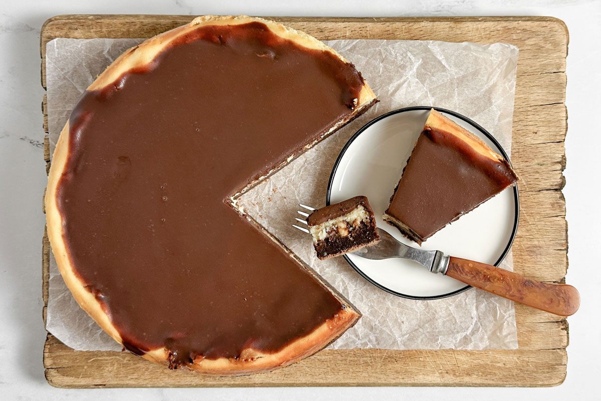 Taste of Home Snickers Cheesecake on a wooden board next to a linen napkin