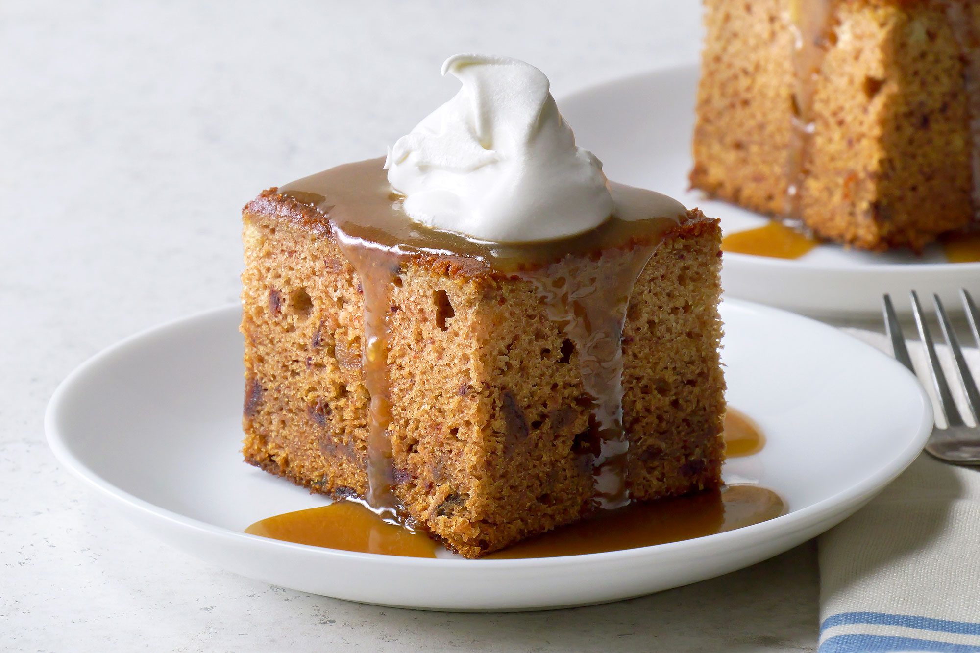 Table view shot of Sticky Toffee Pudding with Butterscotch Sauce; serve on two small plates; with fork and napkins; marble surface;