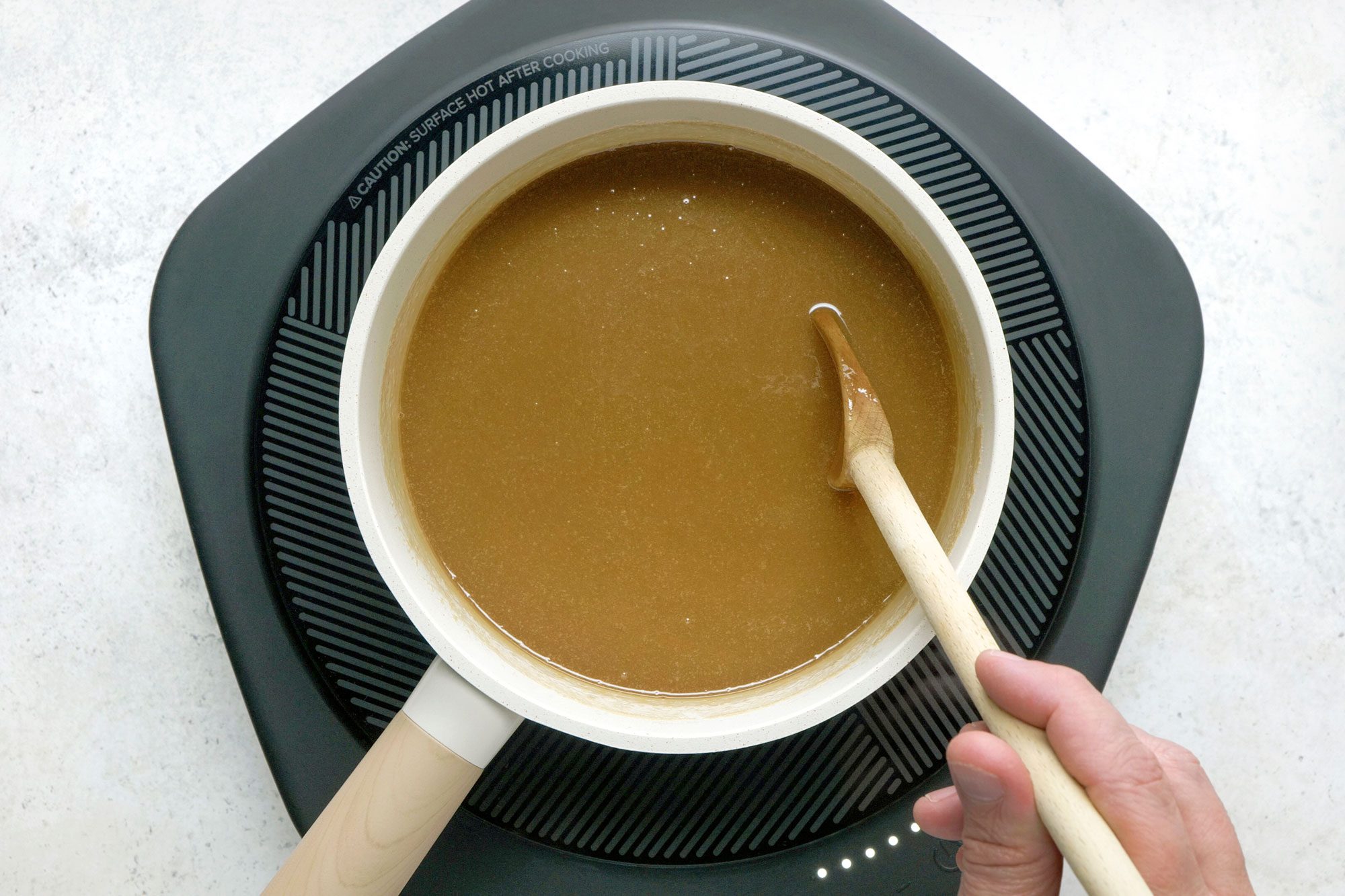 Overhead shot of a small saucepan; melt butter; add brown sugar and half-and-half; bring to a boil over medium heat; stirring constantly; wooden spoon; induction; marble surface;