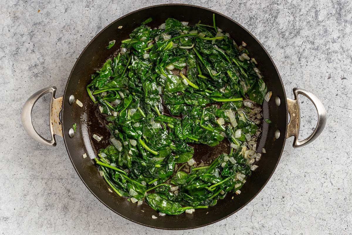 Taste of Home Stuffed Pork Chops photo of the sauteed onion and baby spinach in a skillet.