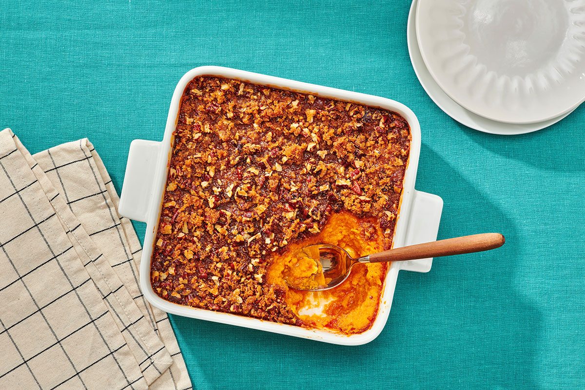 Sweet potato souffle with pecans in a baking dish with a portion removed and a serving spoon in the dish