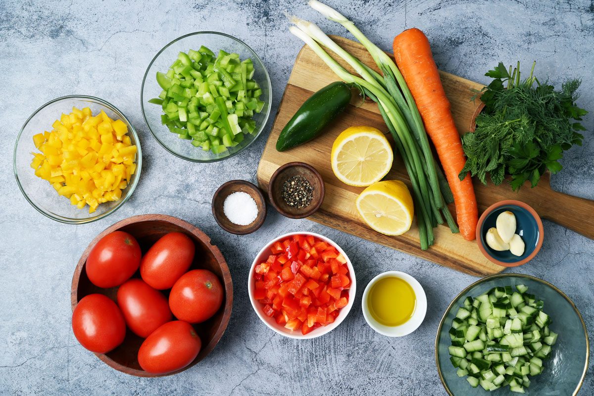 Ingredients for Taste of Home's Israeli Salad in small dishes with a wooden board on a blue surface
