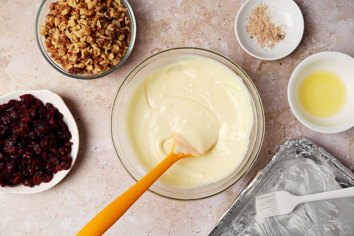 Process shot of the making of Taste of Home's White Chocolate Bark melting white chocolate in a mixing bowl on a beige surface.