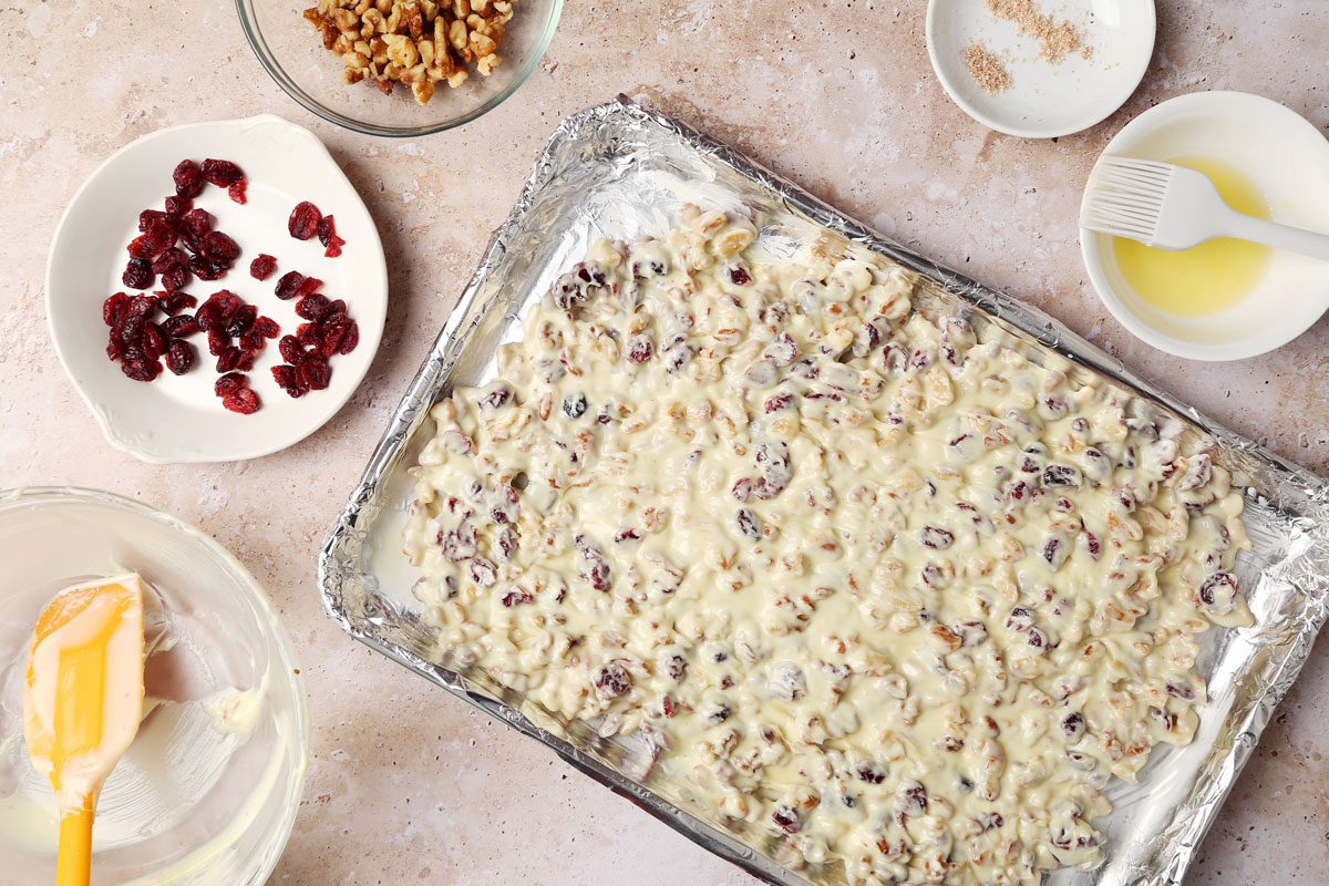 Process shot of the making of Taste of Home's White Chocolate Bark on a baking sheet with ingredients in small bowls.