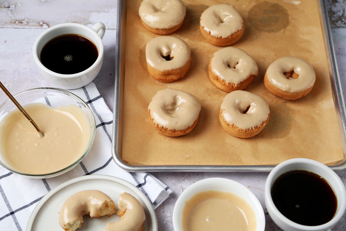 Close up of Taste of Home's Maple Glaze in a bowl with doughnuts on a baking sheet.
