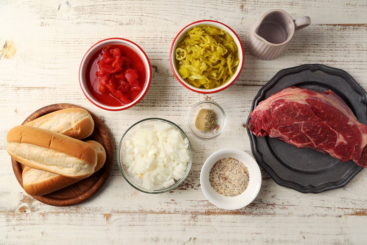 Ingredients for Taste of Home's Italian Beef Sandwiches laid out in small bowls on a white wooden surface.