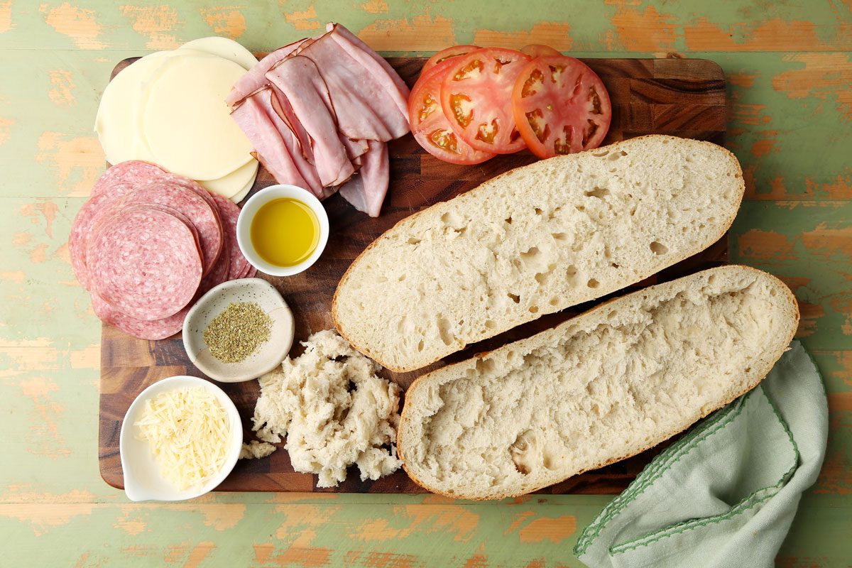 Close up of making Taste of Home's Italian Sub on a wooden board on a green surface.