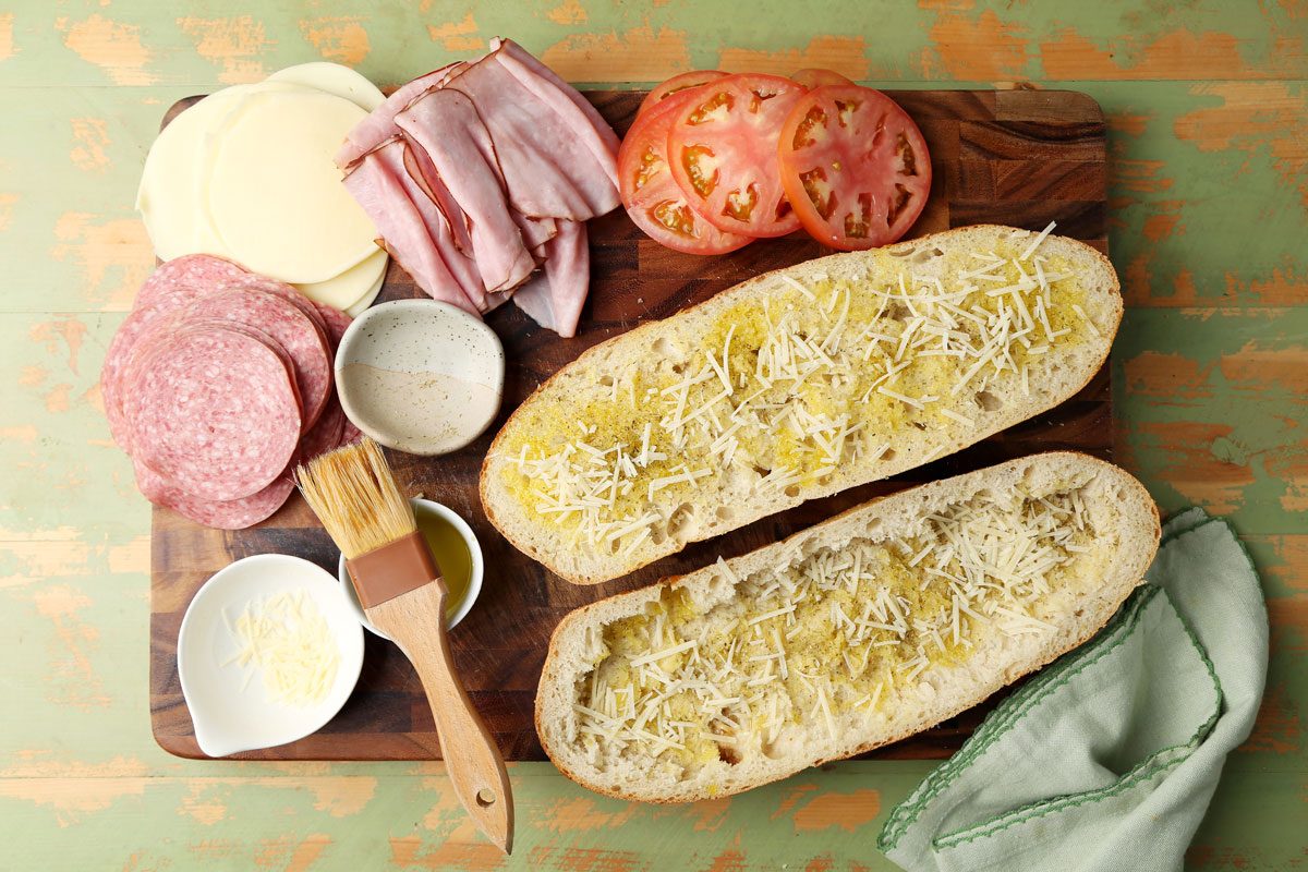 Close up of making Taste of Home's Italian Sub on a wooden board on a green surface.