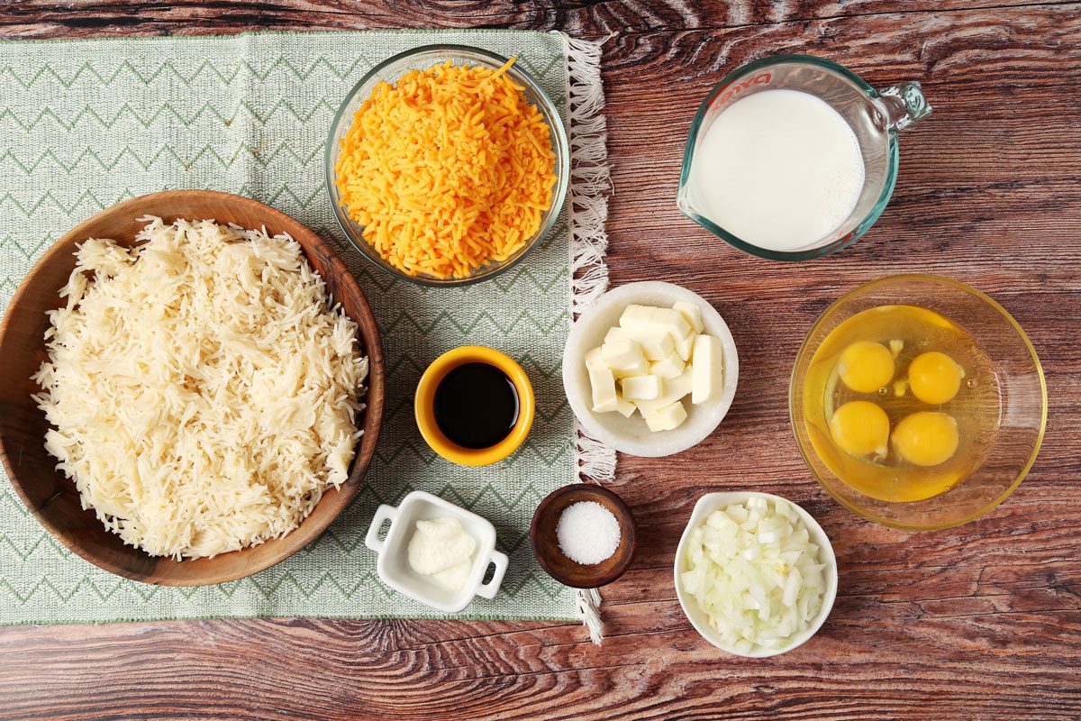 Ingredients for Taste of Home's Cheesy Rice Casserole laid out in small bowls on a brown wooden surface.