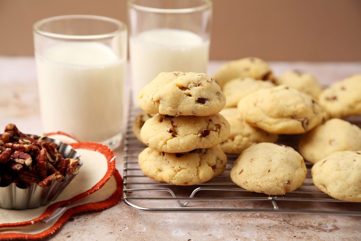 Taste of Home's Butterscotch Cookies on a wire rack with milk on the side and a small bowl of pecans.