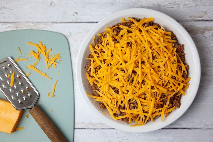 Step 3 of Taste of Home Taco Pie is to transfer the seasoned meat mixture to a greased 9-inch pie plate, spreading it evenly. Sprinkle the shredded cheddar cheese over the top.