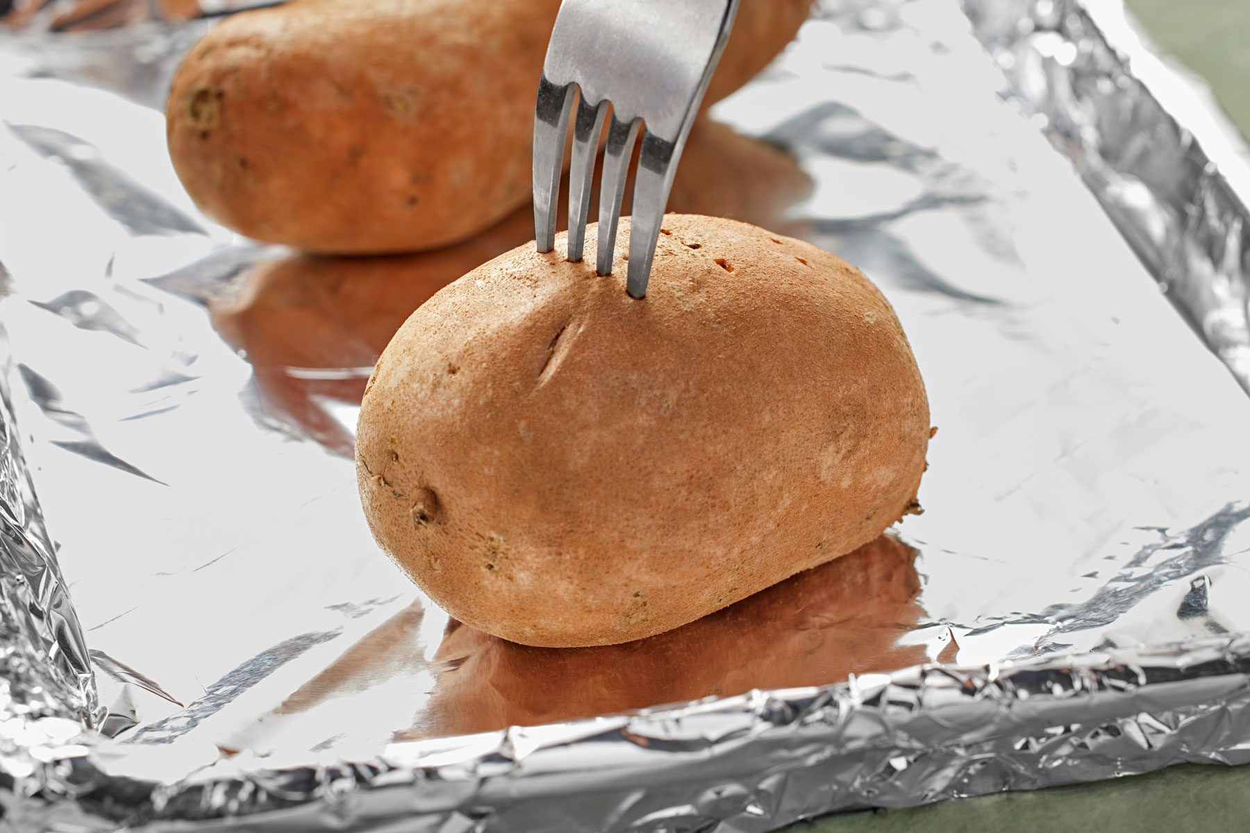 Baked potato on a foil sheet being poked with a fork.