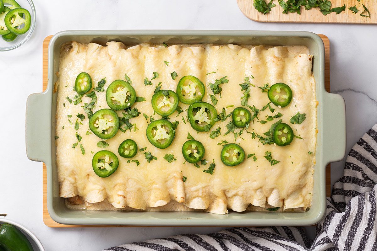 White Chicken Enchiladas in baking dish topped with sliced jalapeños and cilantro