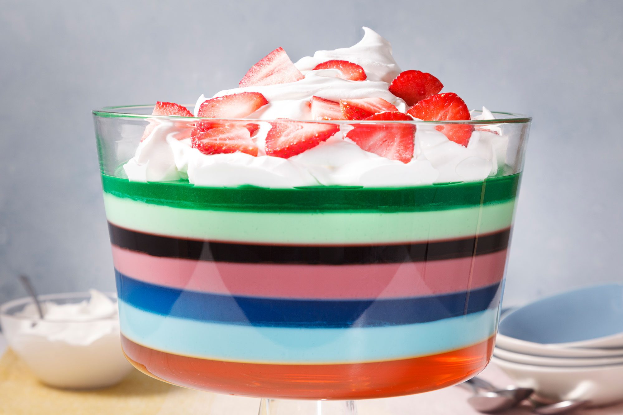 A layered dessert in a glass bowl, topped with whipped cream and strawberries