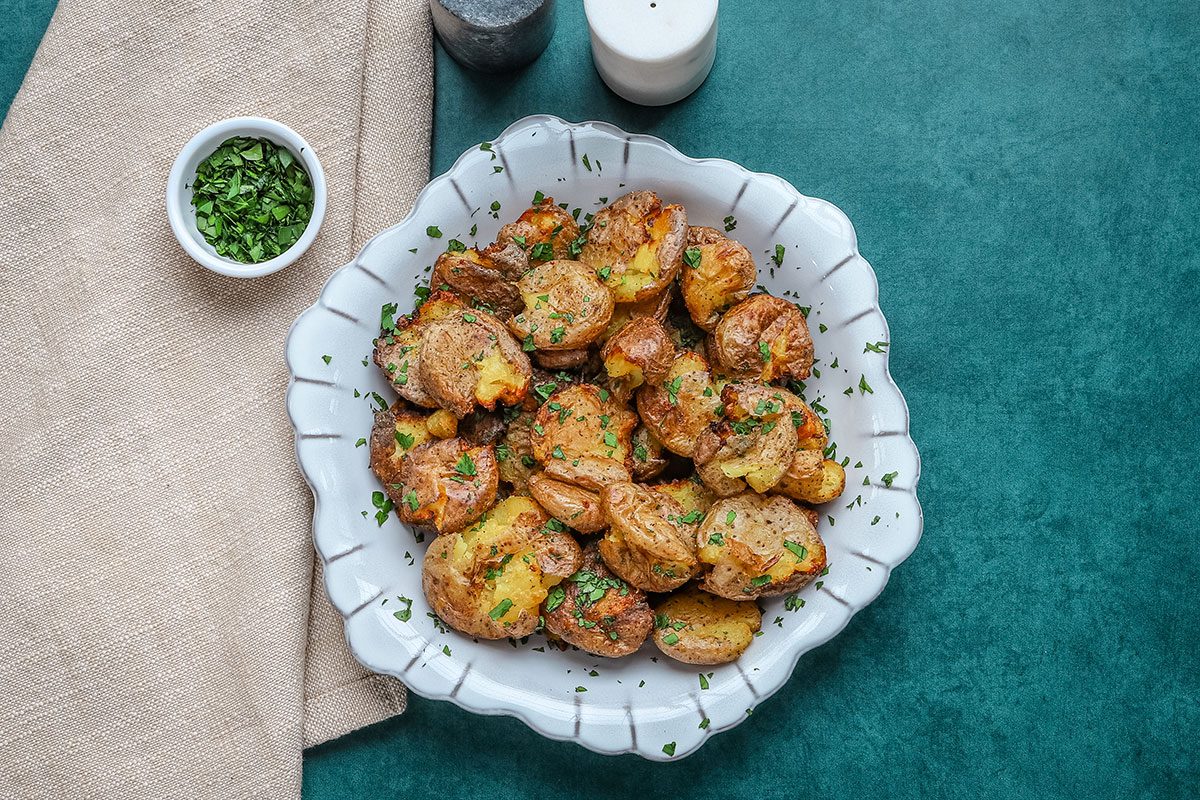 A serving dish with air fryer smashed potatoes with parsley garnish.