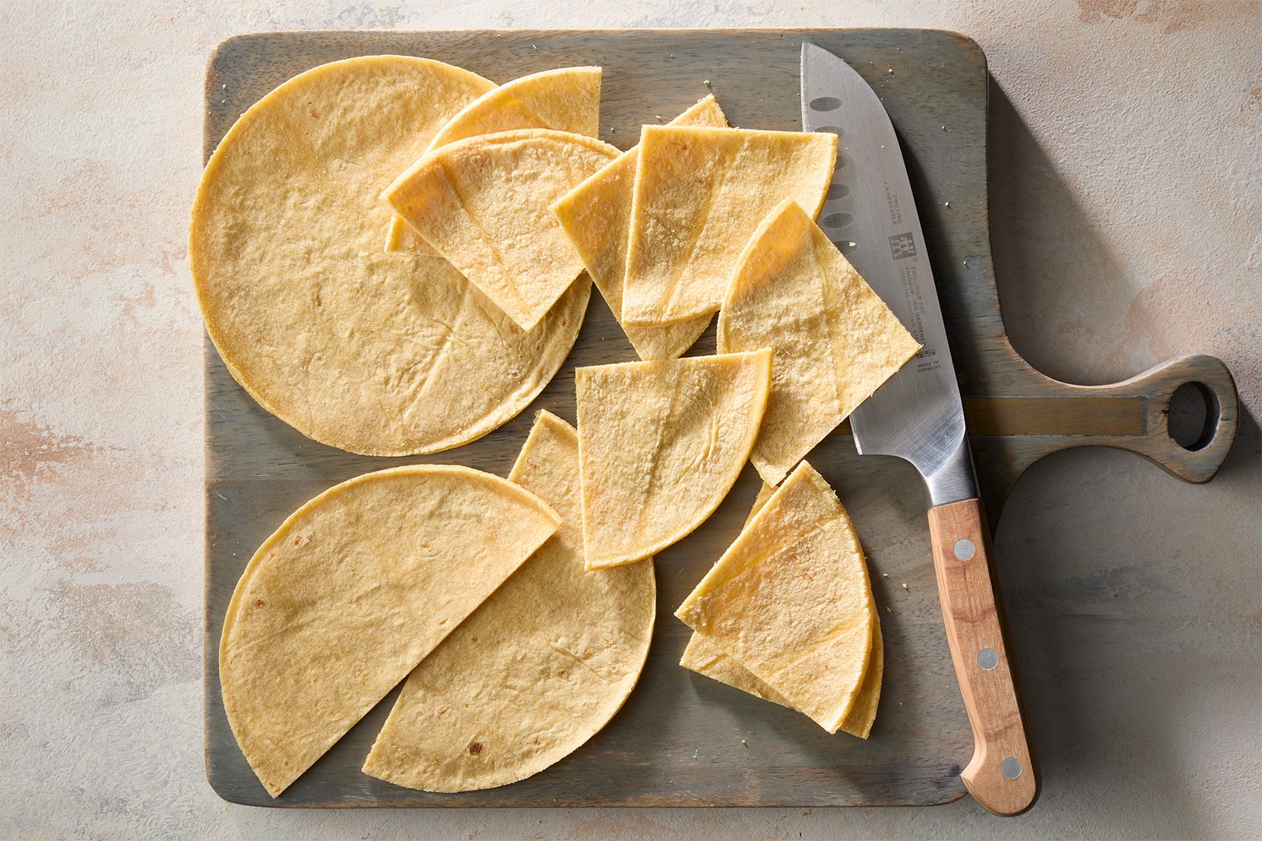 overhead shot of a cutting board with several tortillas on it, There is a knife next to the tortillas, The tortillas are cut into different shapes and sizes, The cutting board is made of wood and has a light brown color;