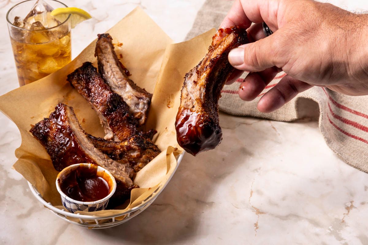 hand holding Air-Fryer Pork Ribs dipped in sauce on marble table shot at a 3/4 view