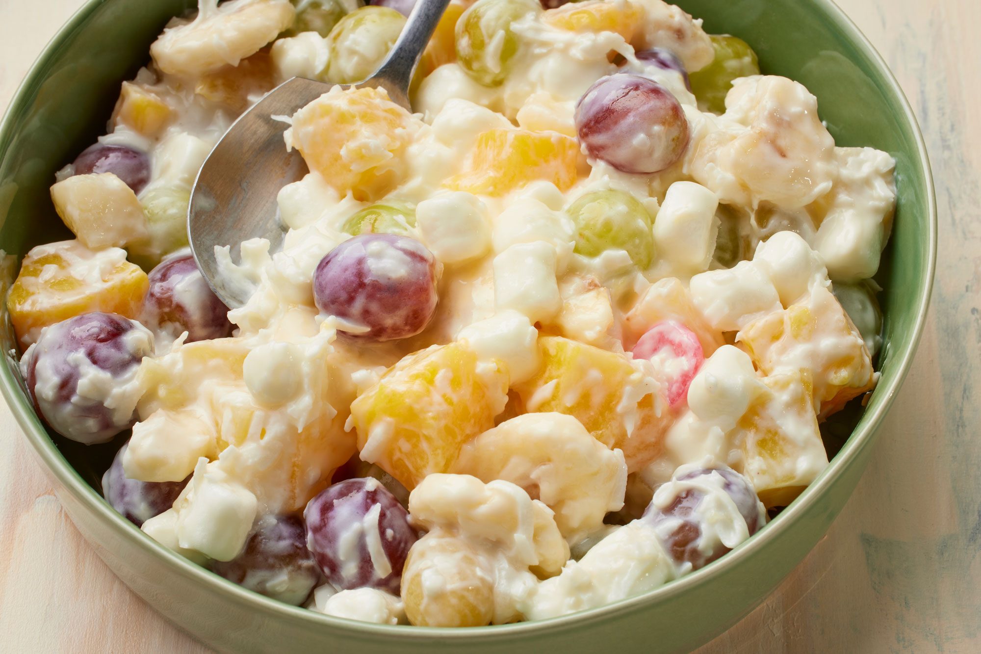 a close up shot of a bowl of Ambrosia Fruit Salad is presented over a wooden background;