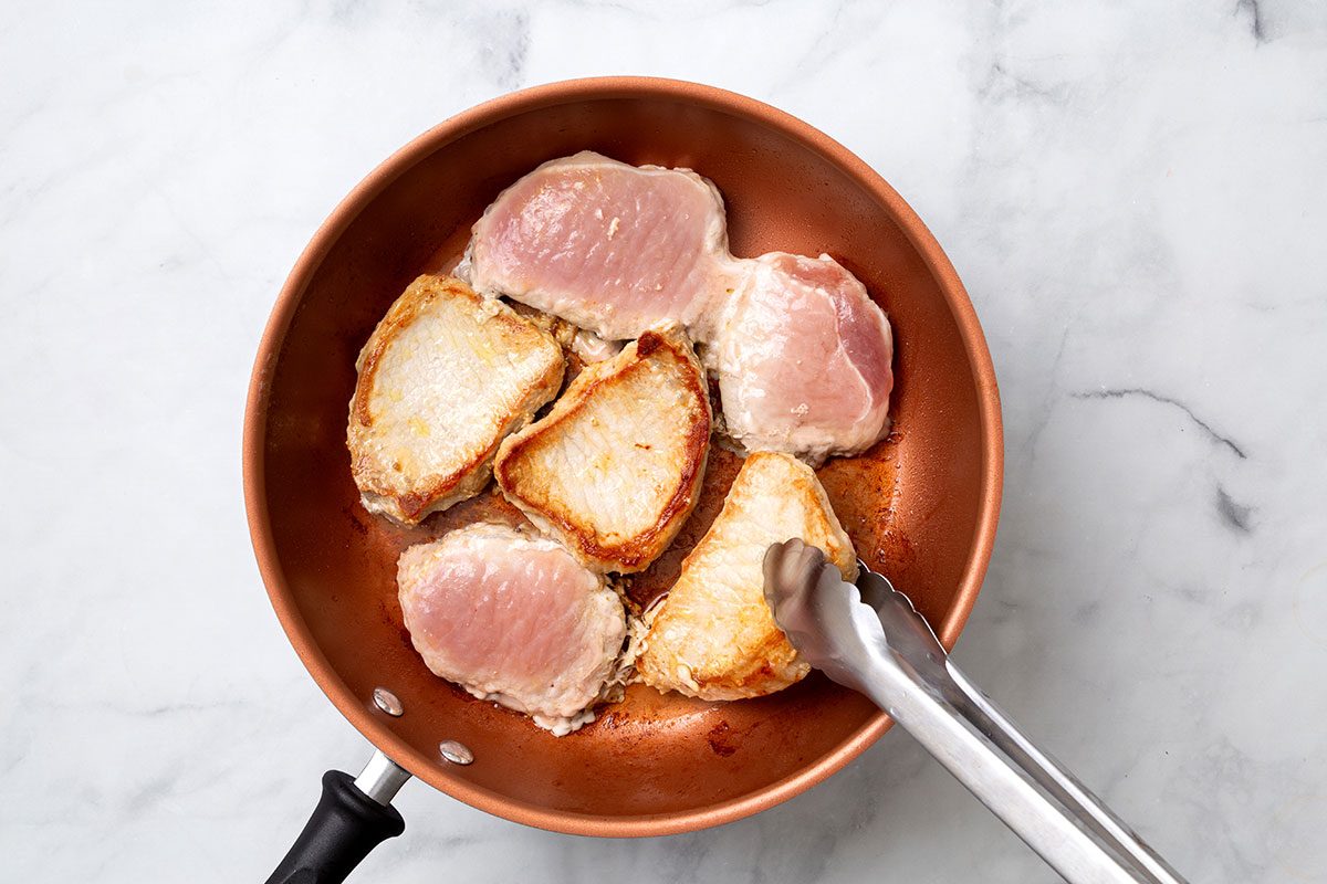 6 Pork chops being browned in a large skillet for step one of Apple Cider Pork Chops recipe for Taste of Home
