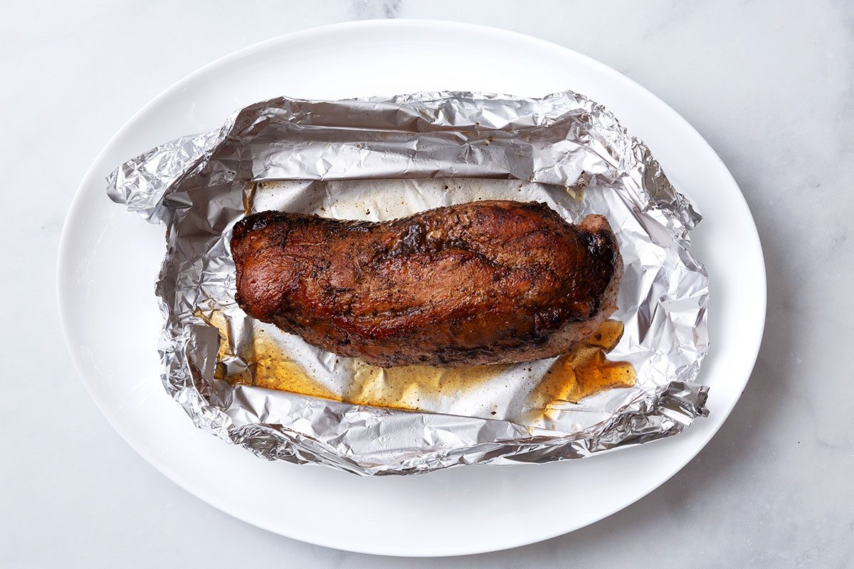 Baked pork tenderloin in foil on a serving platter for step five of Balsamic Pork Tenderloin recipe for Taste of Home