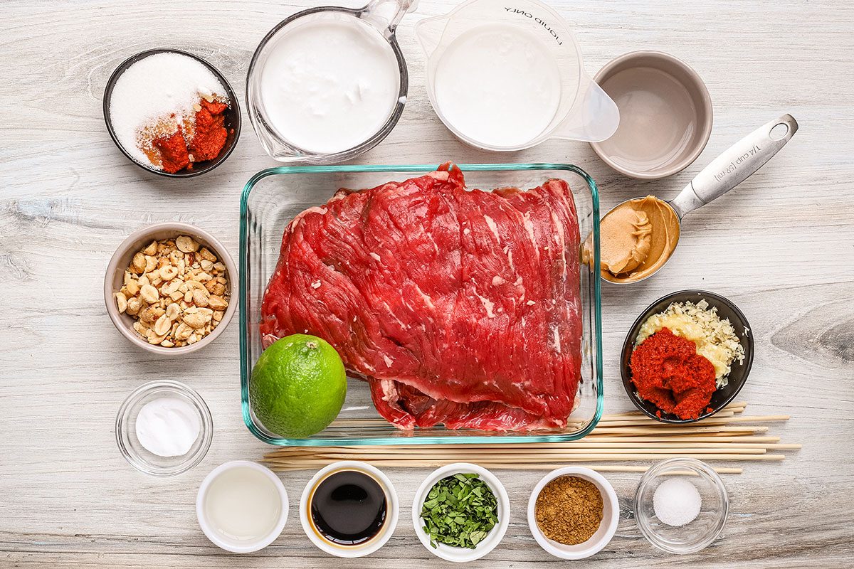 Ingredients for beef satay with peanut sauce, including skirt steak, peanuts, curry paste, and more.