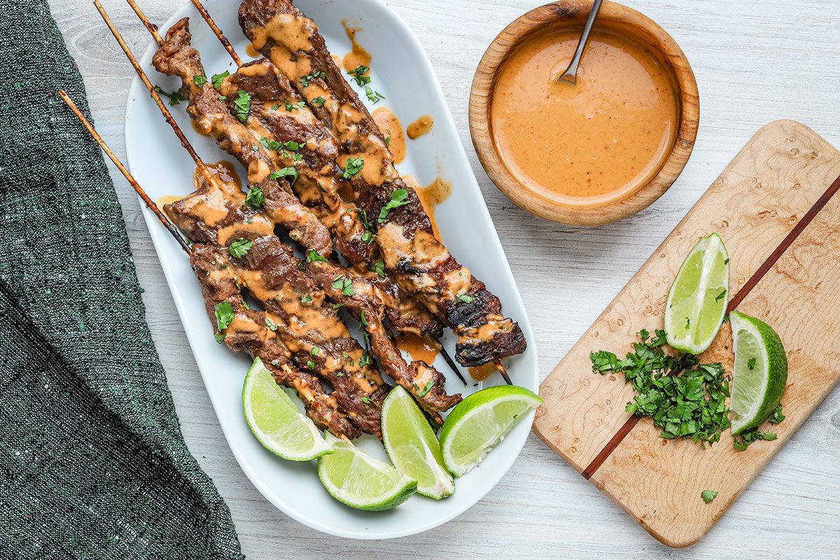 Beef on skewers with limes, cilantro, and peanut sauce.