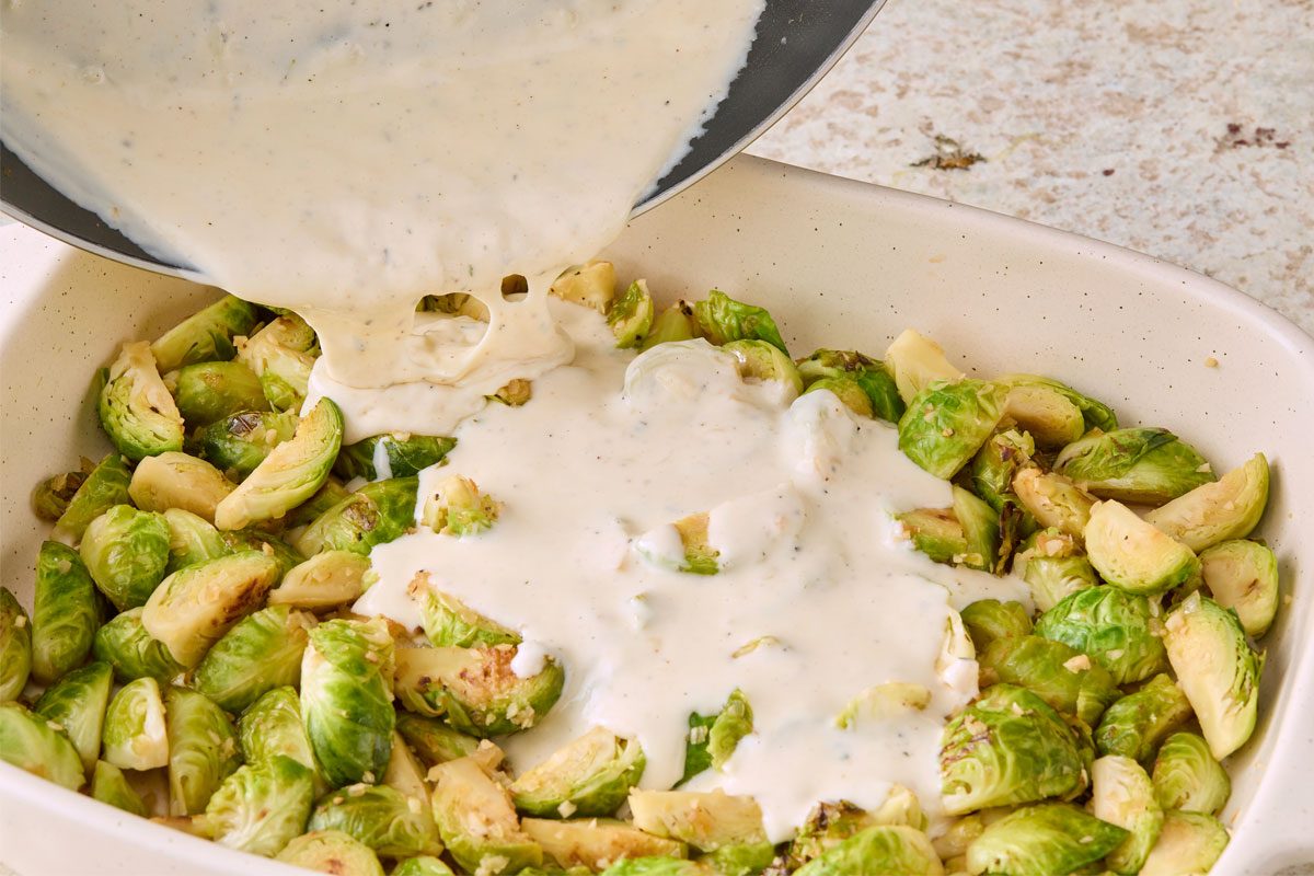 Table view shot of pour sauce over Brussels sprout mixture; stir lightly to combine; marble surface;