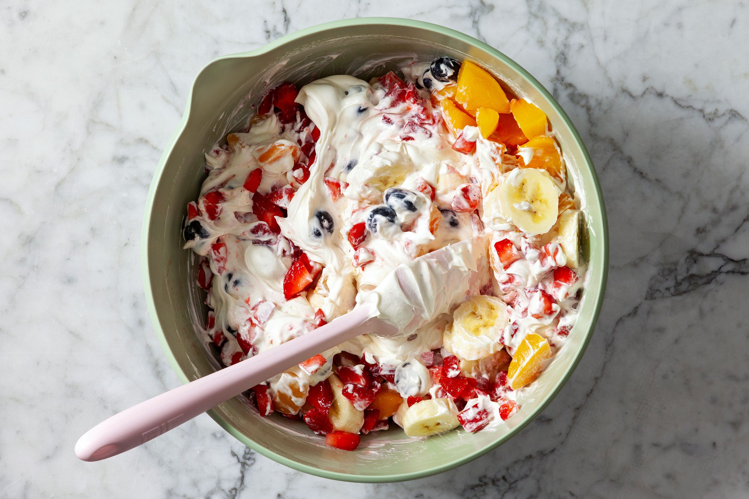 Folding in bananas, peaches, strawberries and blueberries with a sprinkle of graham cracker crumbs to make Cheesecake Fruit Salad