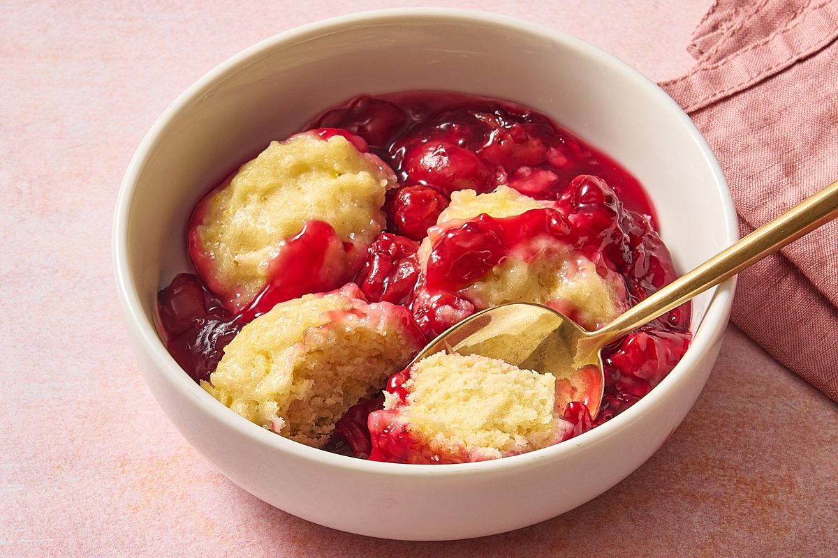 Closeup shot of a bowl of cherry dumplings with one of the dumplings cut in half by a spoon