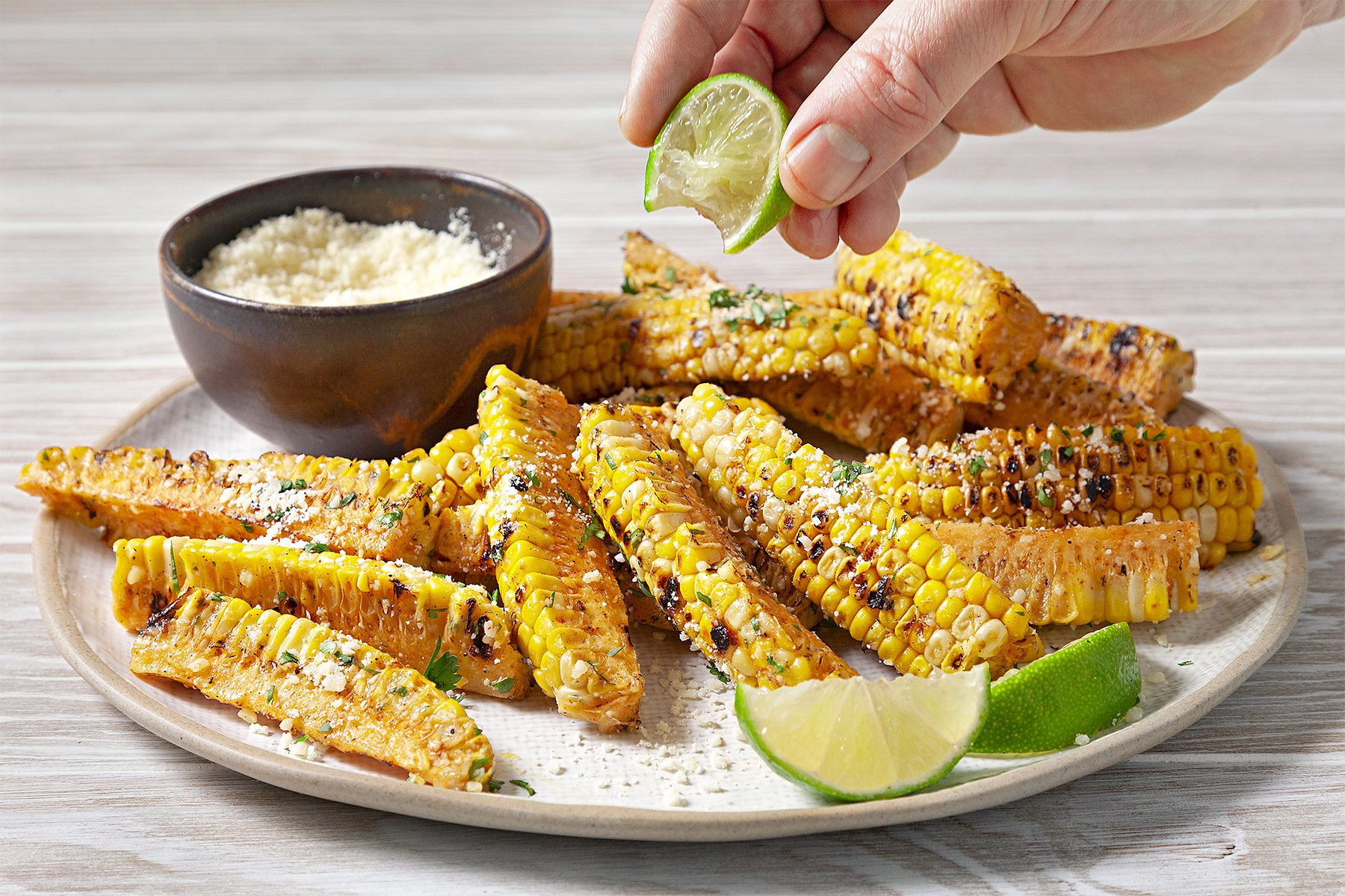 Top view shot of Corn Ribs; serve on large plate with lime wedges; parmesan cheese bowl; fork; wooden surface;
