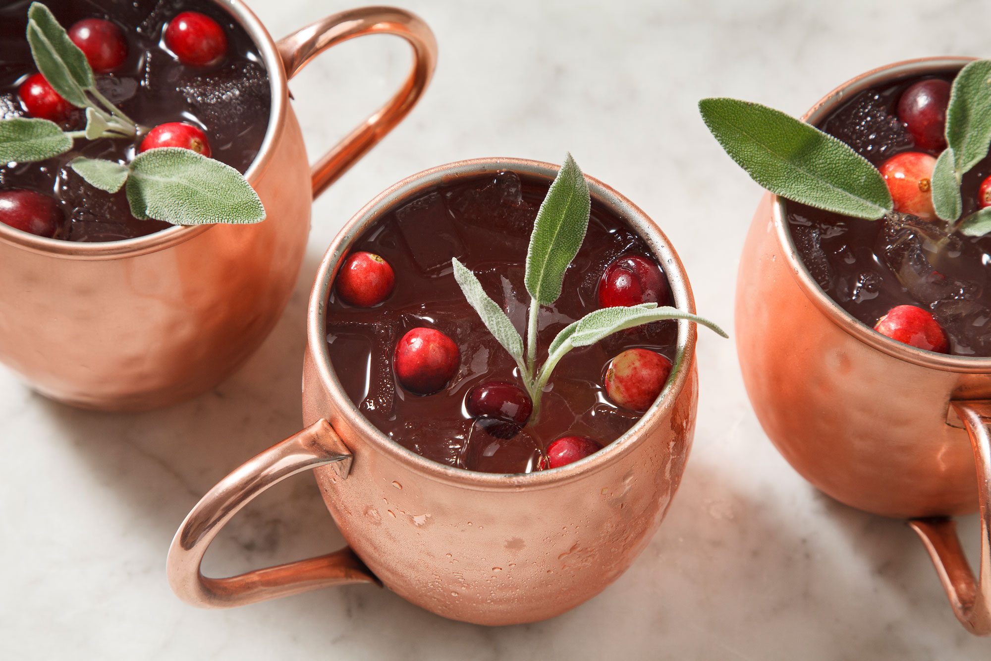 3/4th shot of cranberry moscow mule garnished with frozen cranberries and fresh sage in a copper mug