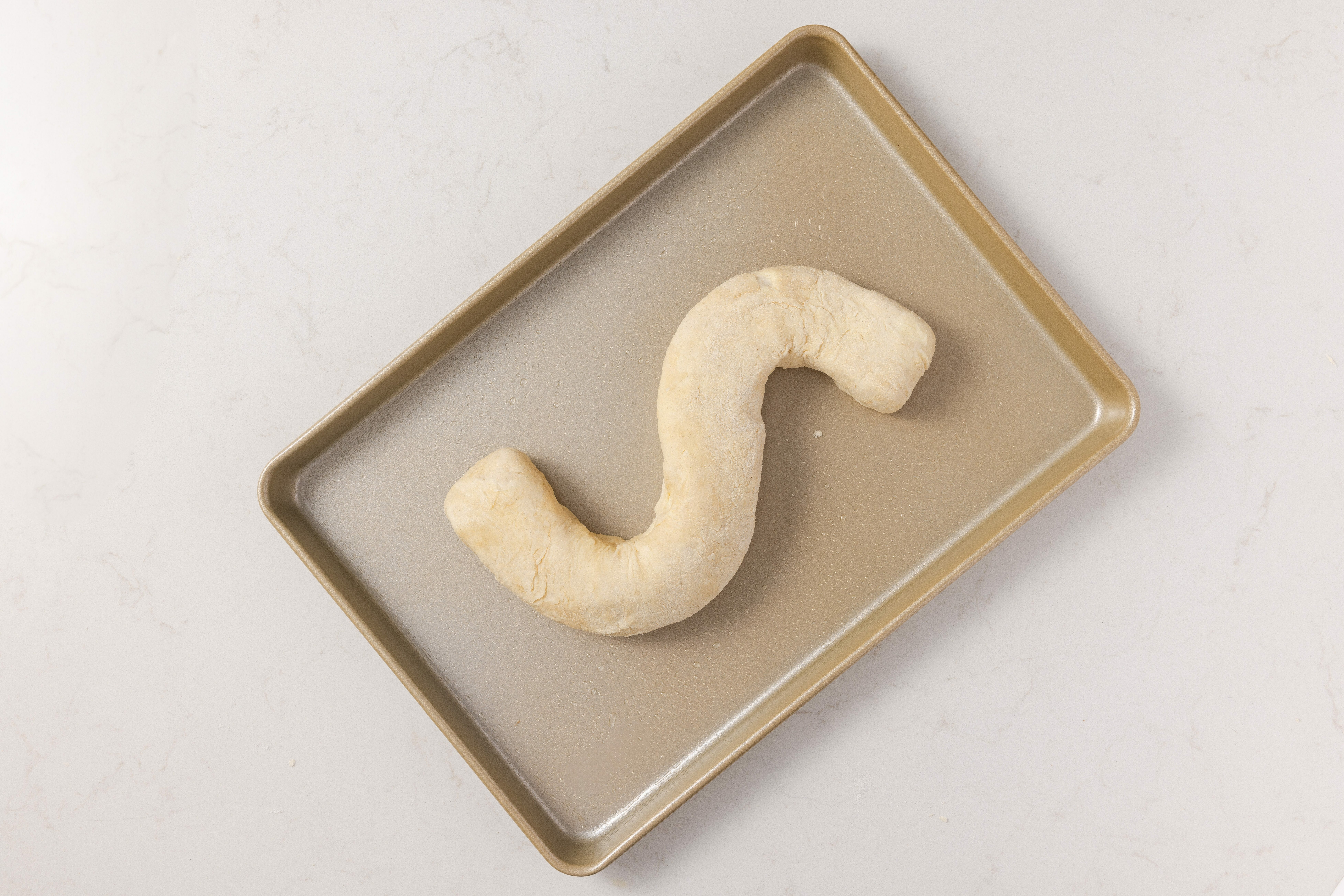 Dough being shaped into an S on baking tray.
