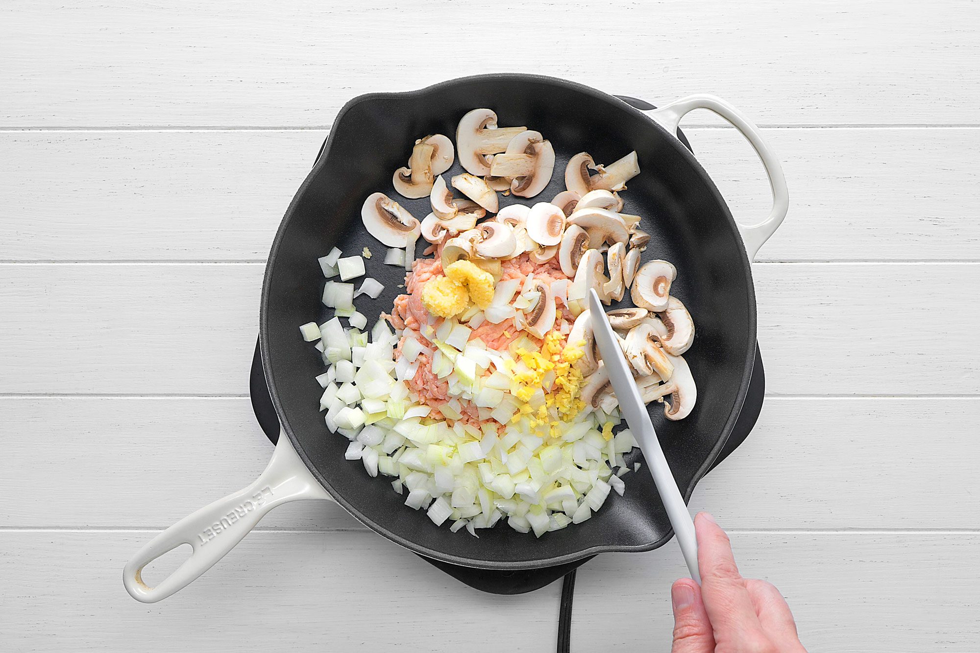 Cast-iron skillet contains a flavorful mixture of ground chicken, chopped onions, mushrooms, and minced garlic