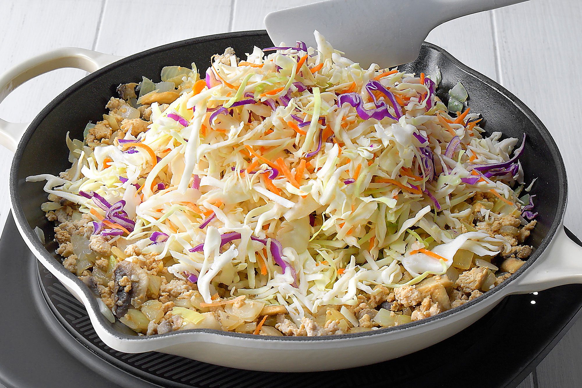Cast-iron skillet contains a mixture of ground chicken, chopped onions, mushrooms, and shredded cabbage, The cabbage is a mix of green and purple varieties