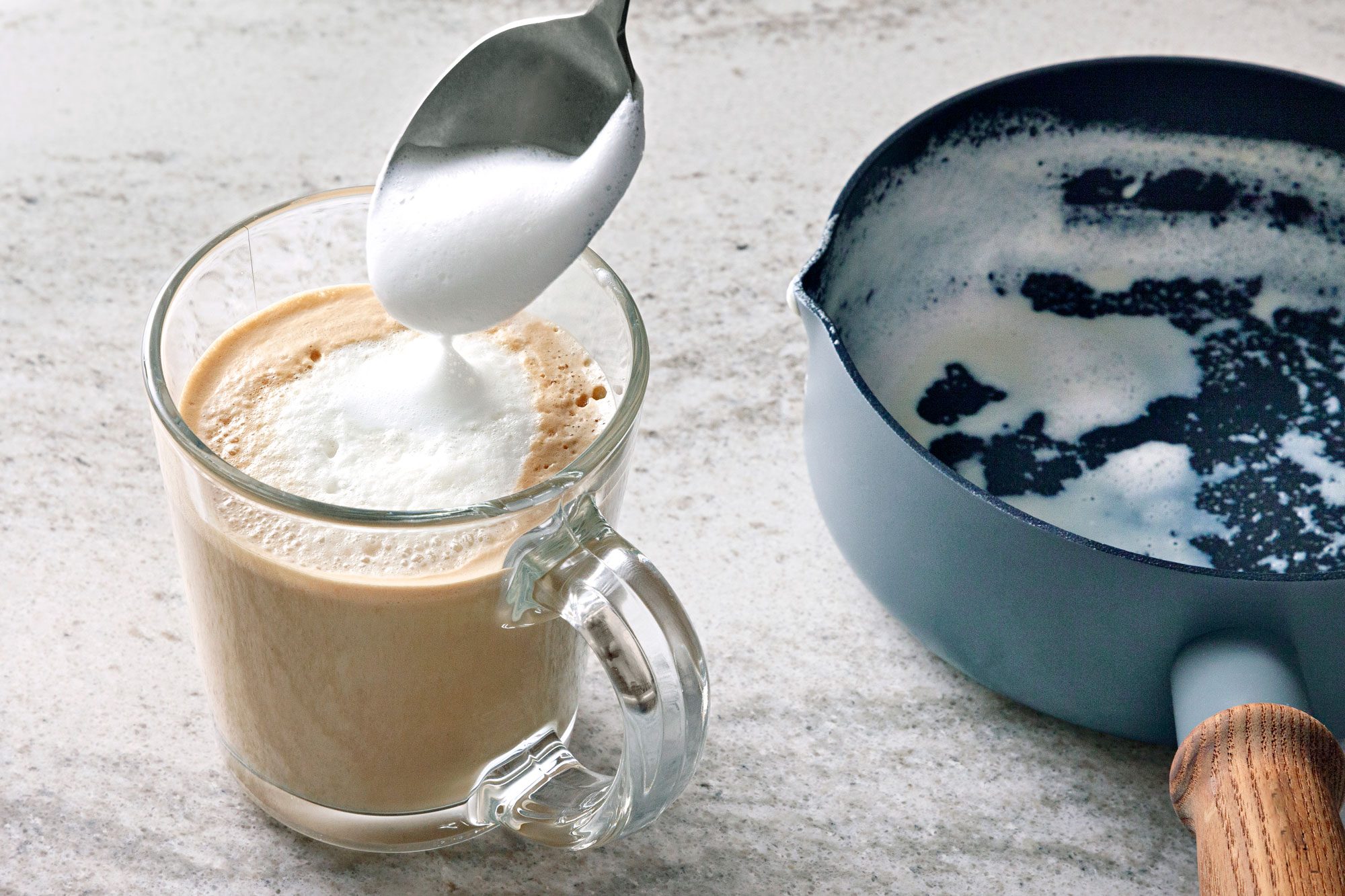 A glass of latte with a spoon of frothed milk being poured into it