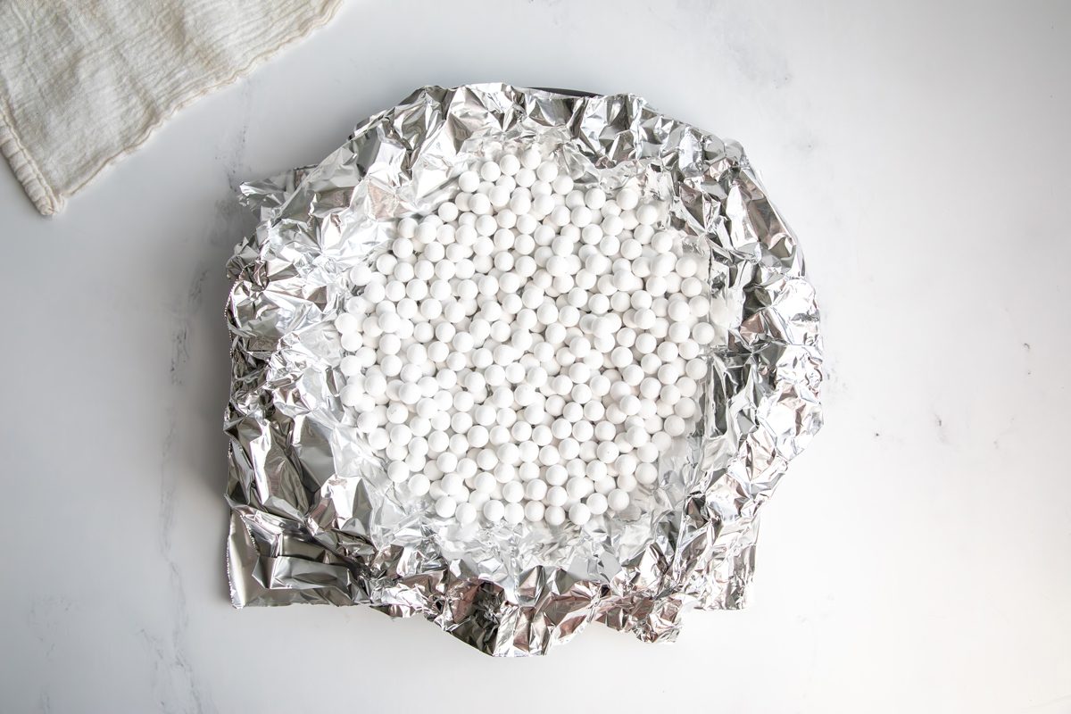 Overhead shot for Taste of Home Fudge Pie, unbaked crust in a pie tin with tin foil and pie beads.