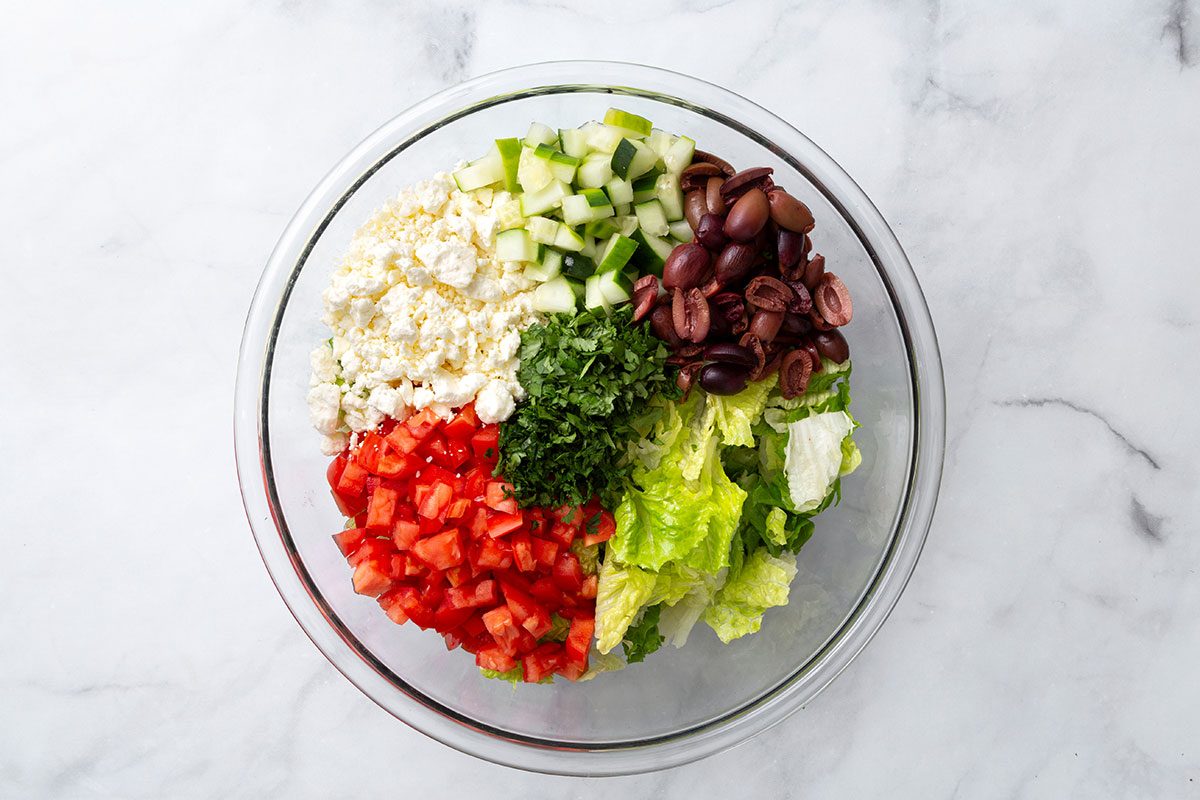Chopped romaine, plum tomatoes, greek olives, parsley, cilantro, cucumber and feta cheese in a mixing bowl for step one for Greek Salad with Lettuce recipe for Taste of Home