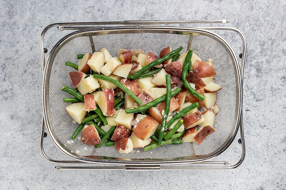 cooked potatoes and green beans draining in a colander.