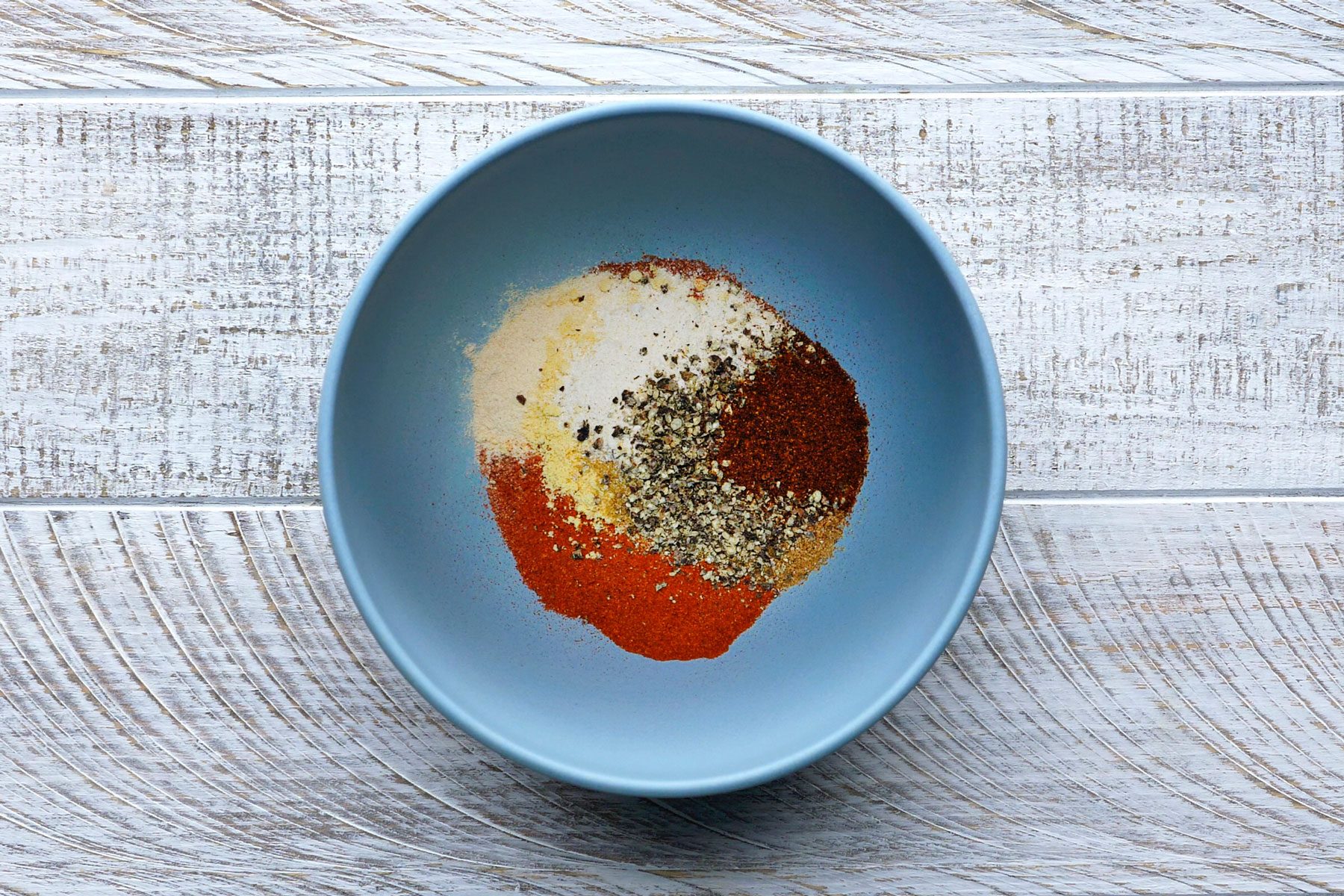 Paprika, garlic powder, onion powder, cumin, mustard, black pepper and ground chipotle pepper mixed in a small bowl.