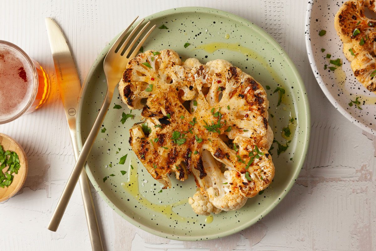 Two single servings of Taste of Home Grilled Cauliflower Steaks on green and white plates, garnished with parsley