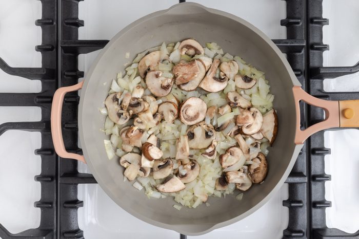 Onions and mushrooms being cooked in skillet.