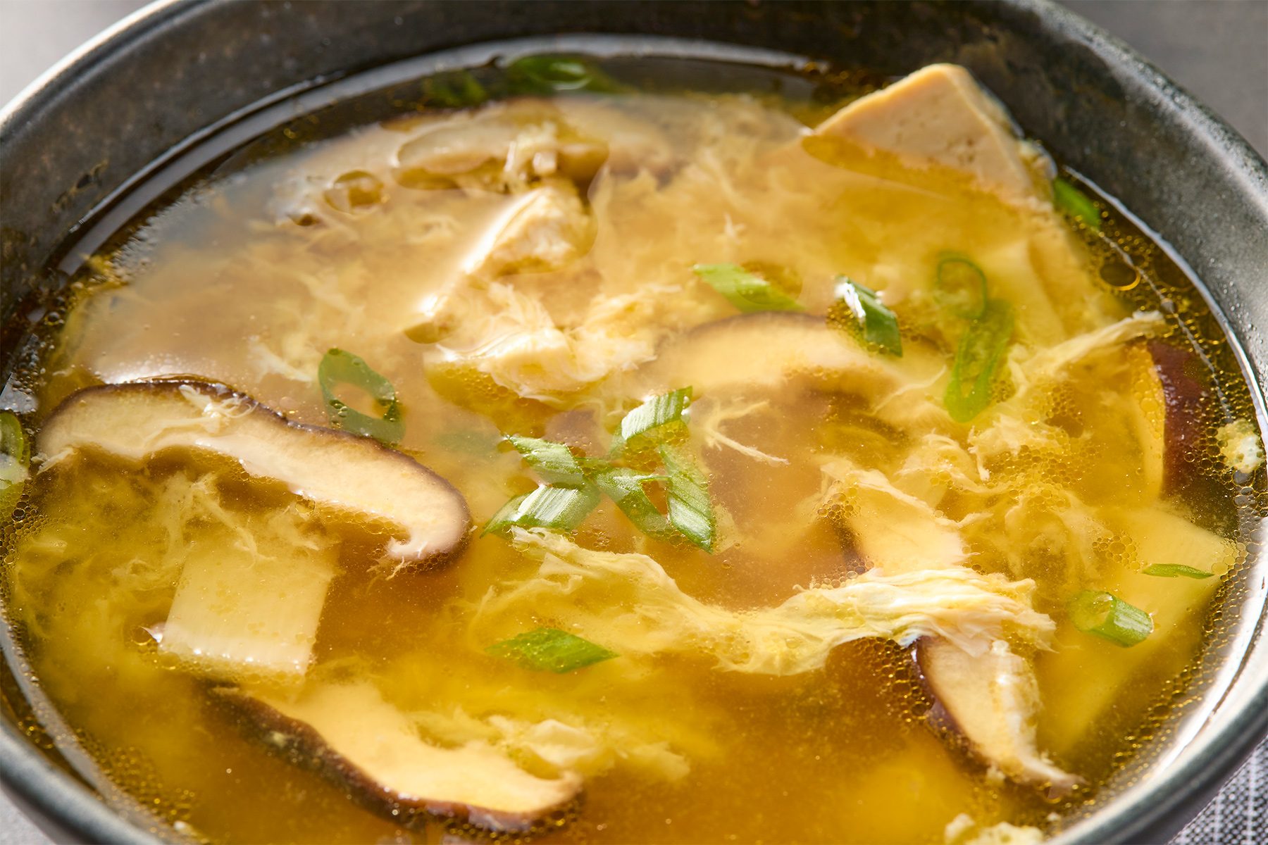 Close shot of Easy Hot and Sour Soup; serve soup in bowl;; top with green onion;