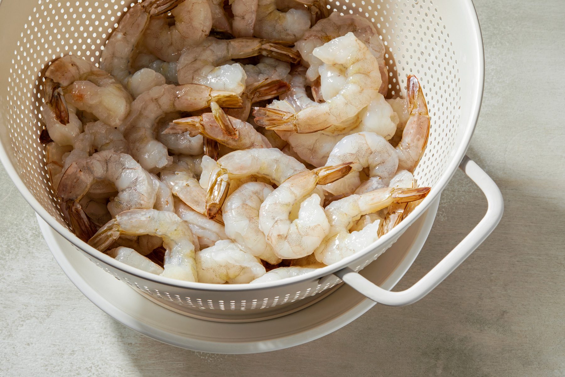 3/4 shot of frozen shrimp in a colander being rinsed with water.