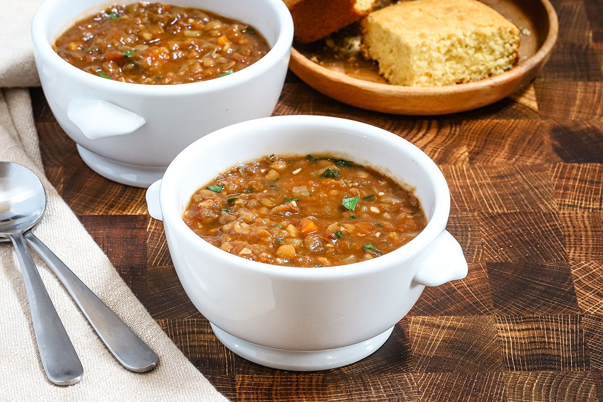 Instant Pot lentil soup in bowls with a parsley garnish and cornbread in the background.