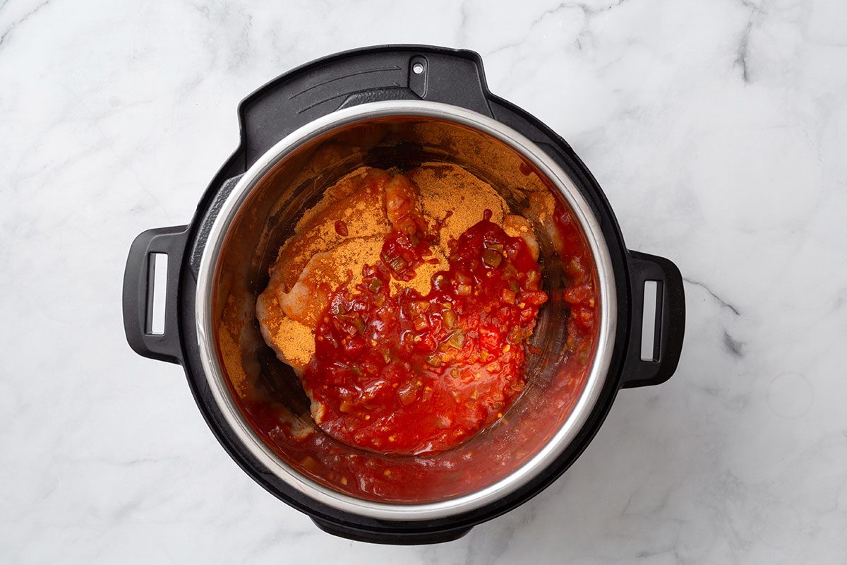 Taco seasoning sprinkled over chicken breasts and topped with salsa in a pressure cooker for step one of Instant Pot Salsa Chicken recipe for Taste of Home