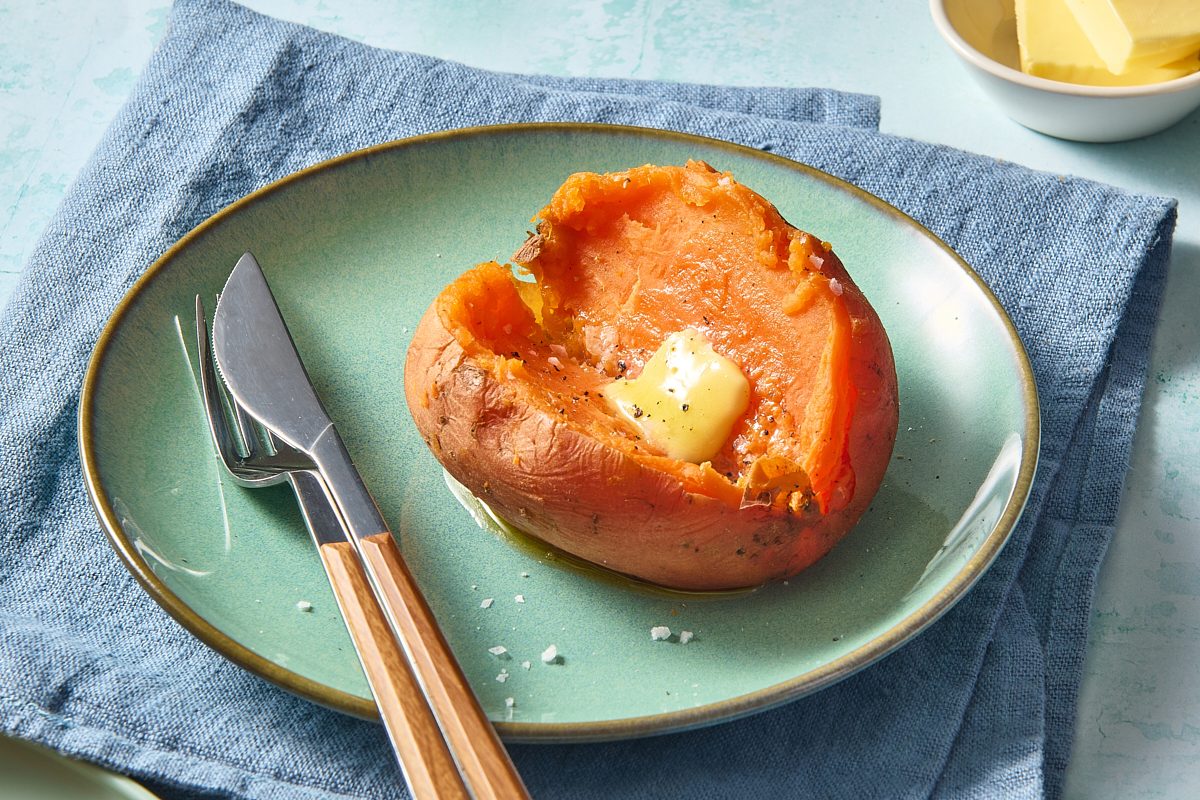 Closeup of a single instant pot sweet potato topped with butter, served on a plate with a knife and fork