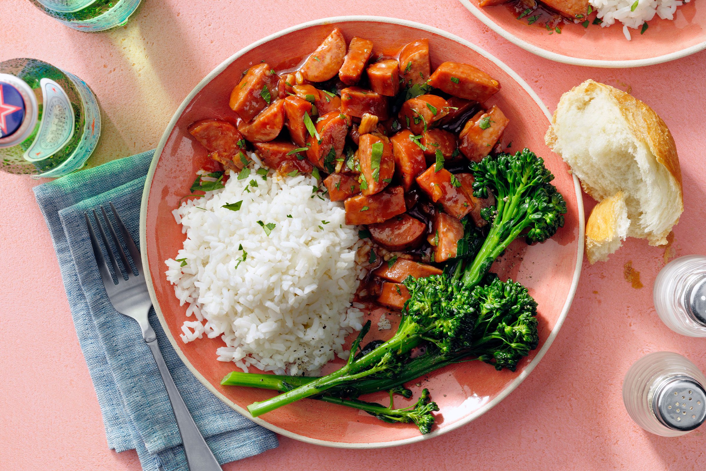 A dish containing Keilbasa and rice served on a plate with fresh green leafy vegetable