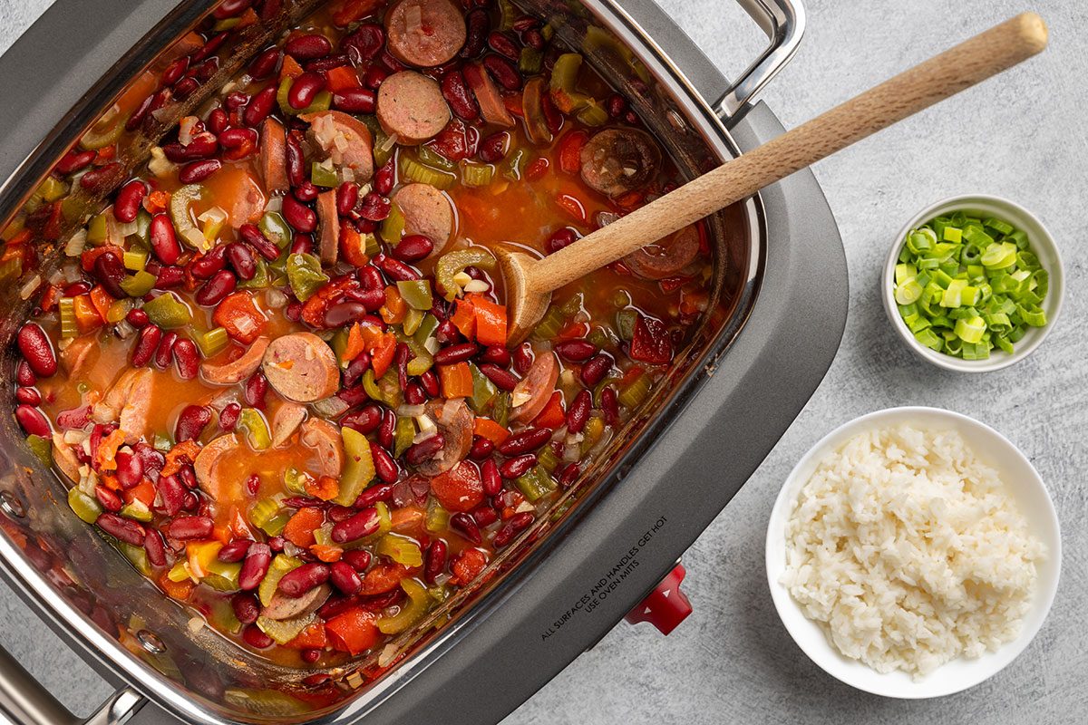 Louisiana Red Beans and Rice in slow cooker with rice and green onions for serving.